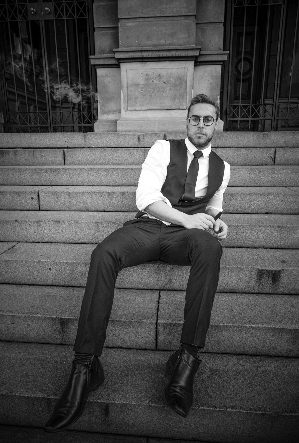 Groom Ruan resting on the stairs, taking a seat whilst vaping in the coolest black and white image.