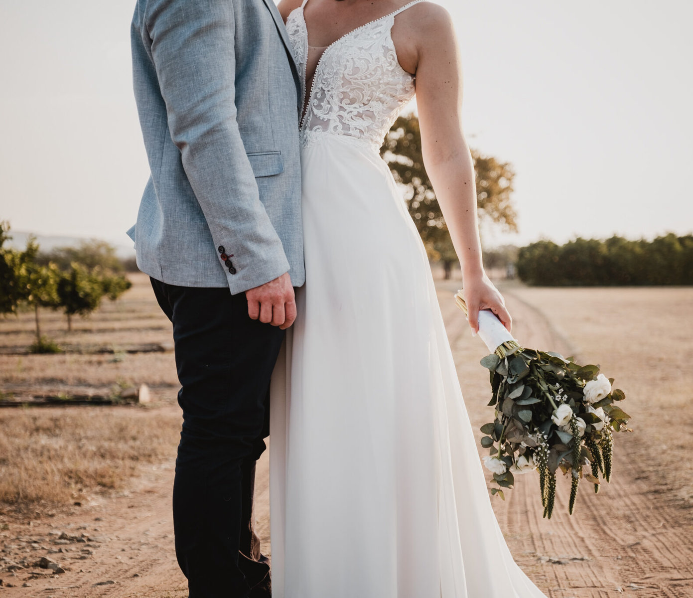 Photo by Lynette van der Bijl Close up image of the groom and bride with the focus on the flowers and them standing on a dirt road at their farm wedding.