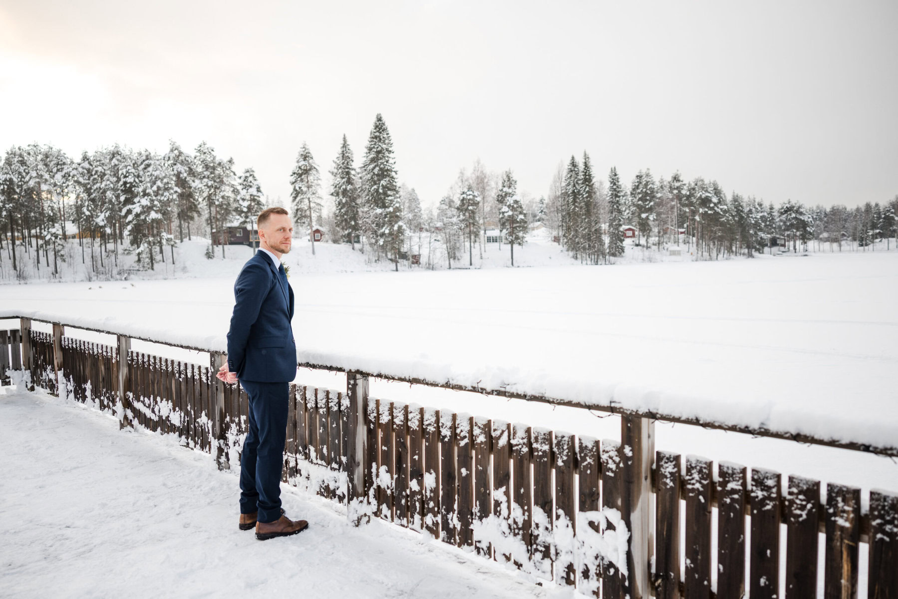 Man in navy suit overlooking snowy landscape in Sweden.